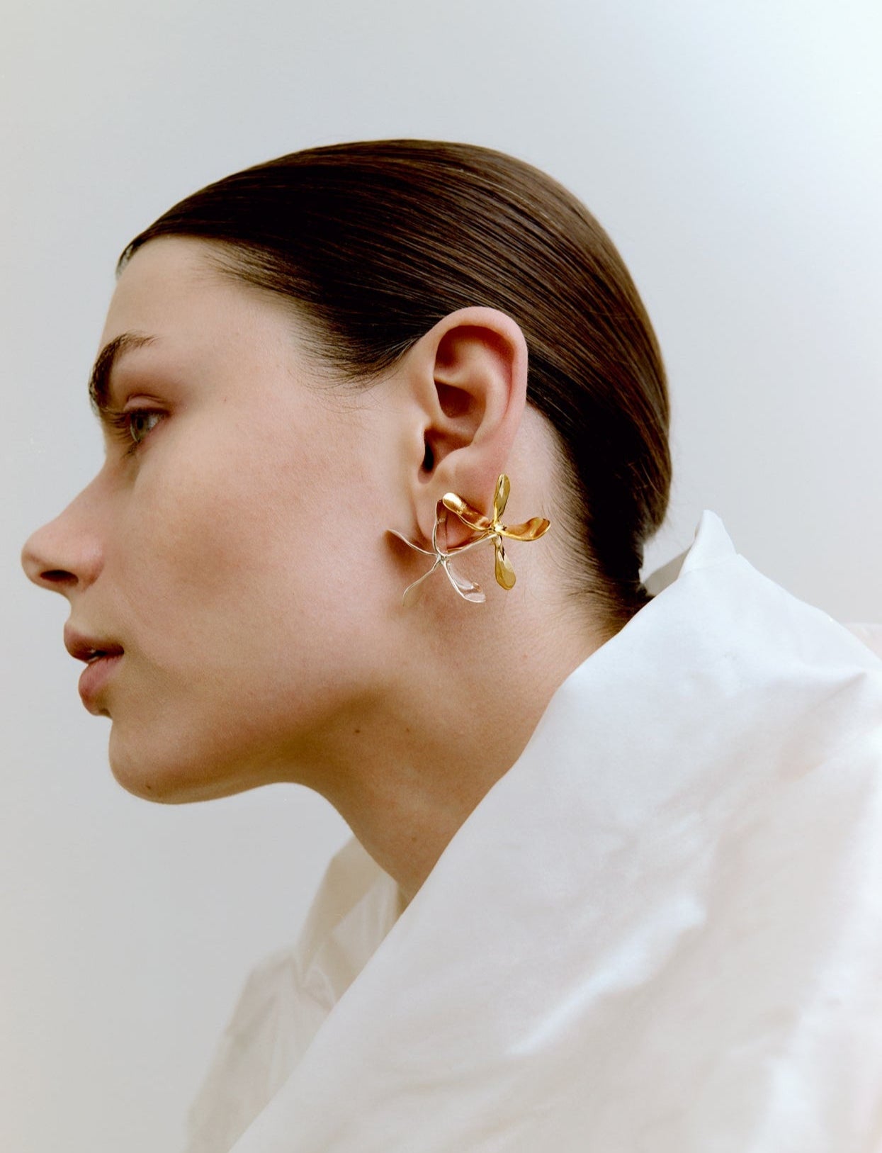 Woman wearing a gold and a silver earring against a white background