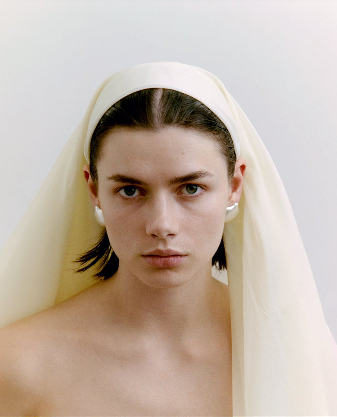 Woman wearing a white headscarf and silver earrings against a plain background