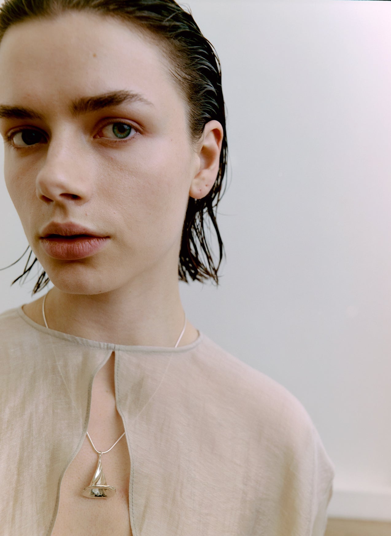 Person wearing a beige top and necklace with a minimal background