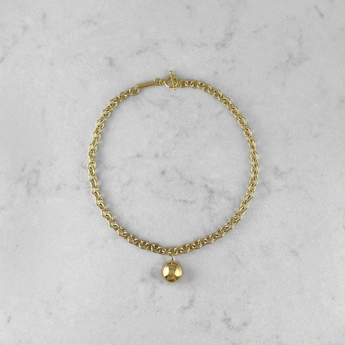 Product photo of a gold chain necklace with pendant, laying on a marble plate