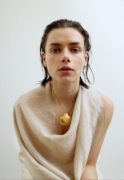 Person wearing a beige scarf and gold necklace against a plain background