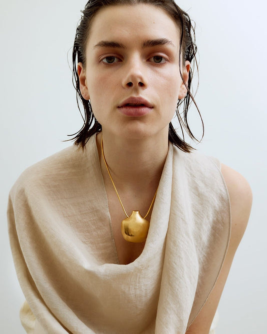 Person wearing a beige scarf and gold necklace against a plain background