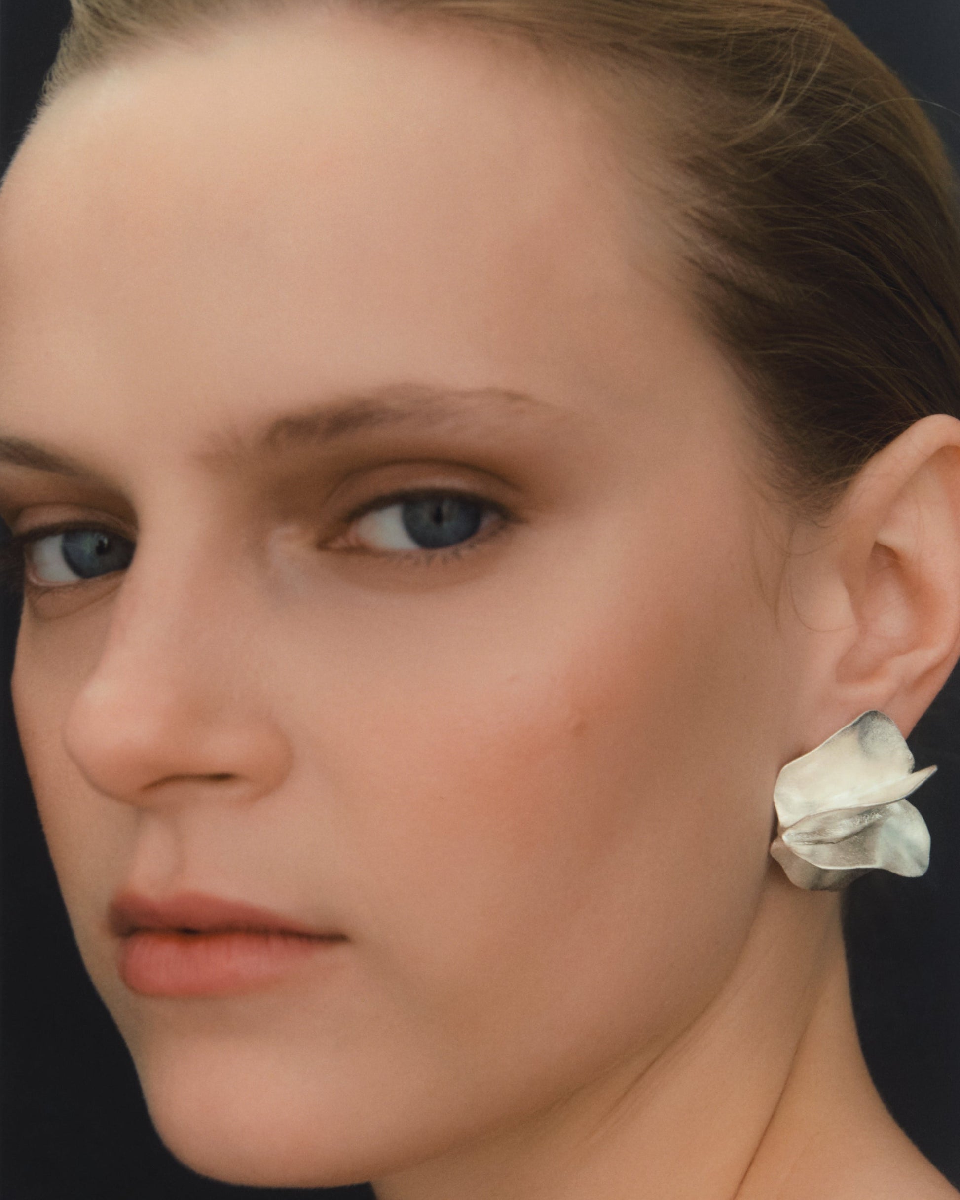 Close-up portrait of a woman wearing a single sculptural earring made from silver.