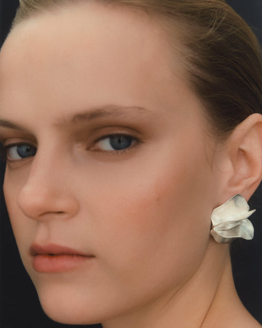 Close-up portrait of a woman wearing a single sculptural earring made from silver.