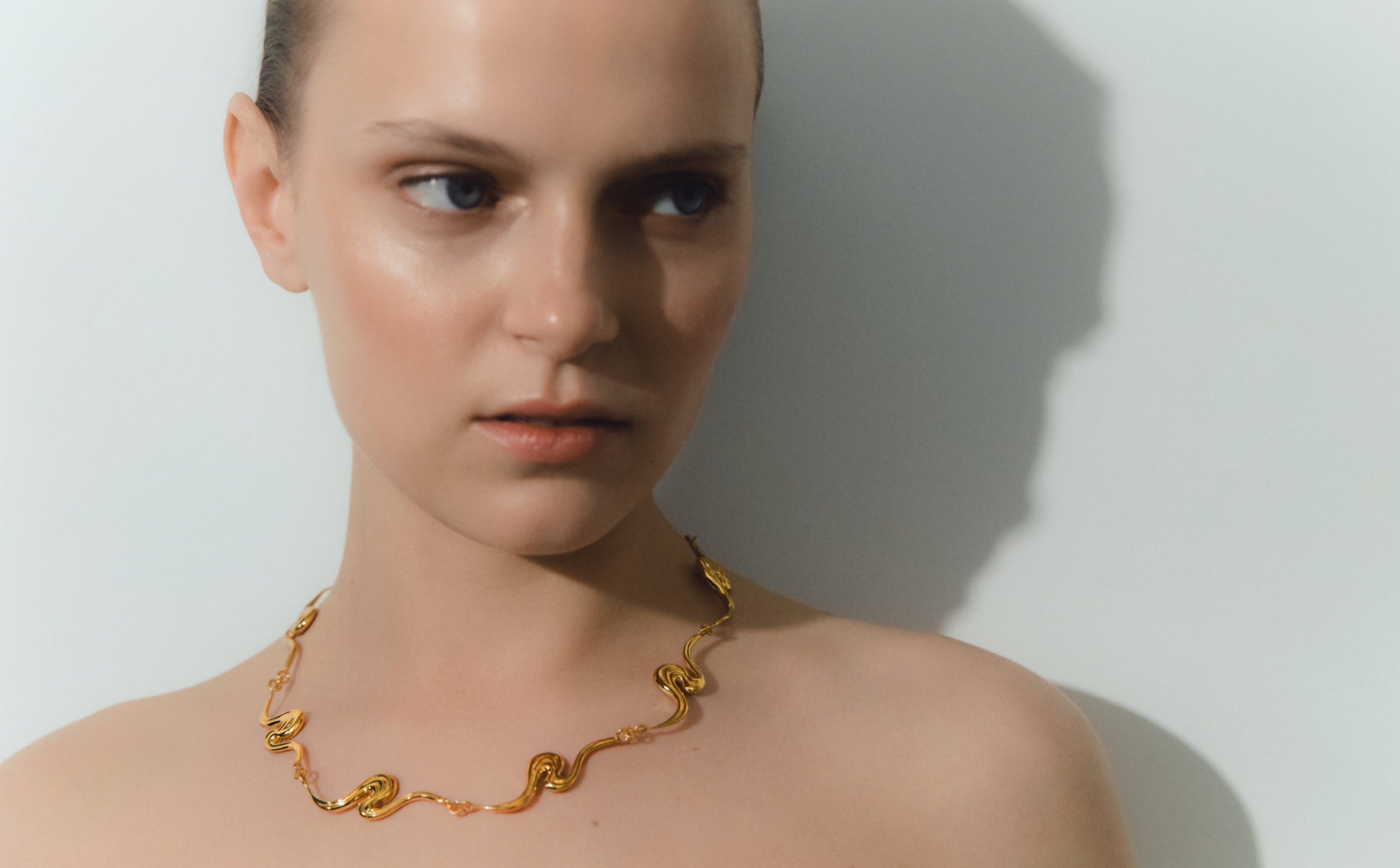 A close-up lifestyle shot of a model wearing a gold chain necklace, set against a plain light gray background.