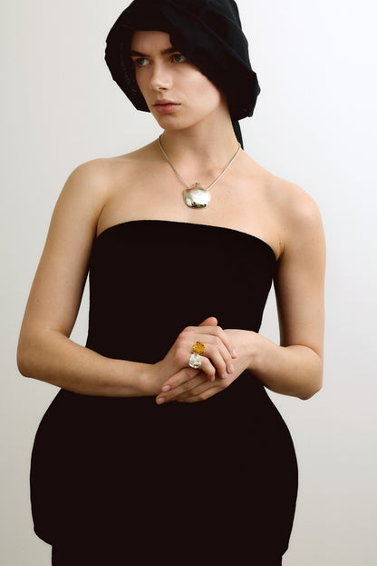 Woman wearing a black strapless dress, jewelry and headscarf against a plain background
