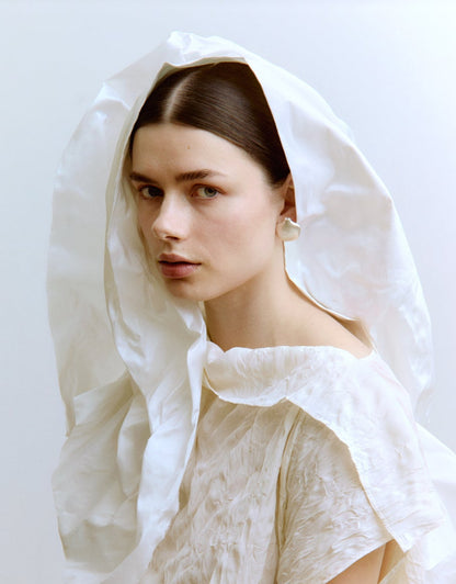 Woman wearing a white lace dress and silver earrings against a light background