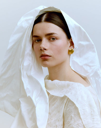 Woman wearing a white headscarf and gold earrings against a plain background
