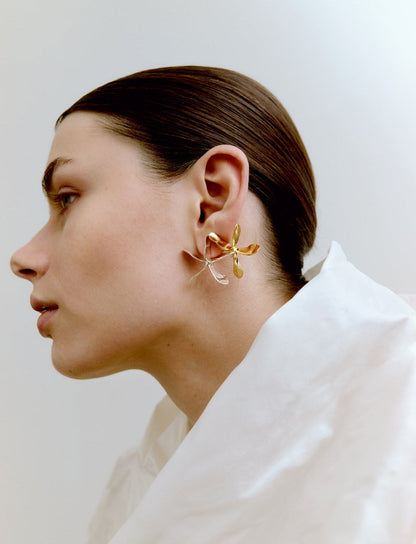 Woman wearing a gold and a silver earring against a white background