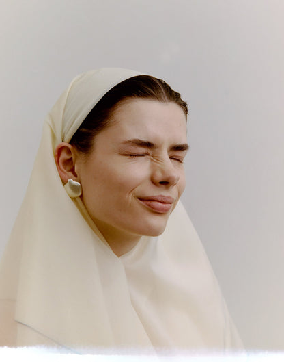Woman wearing a beige headscarf and silver earrings against a plain background