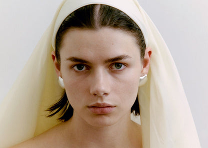 Woman wearing a white headscarf and silver earrings against a plain background