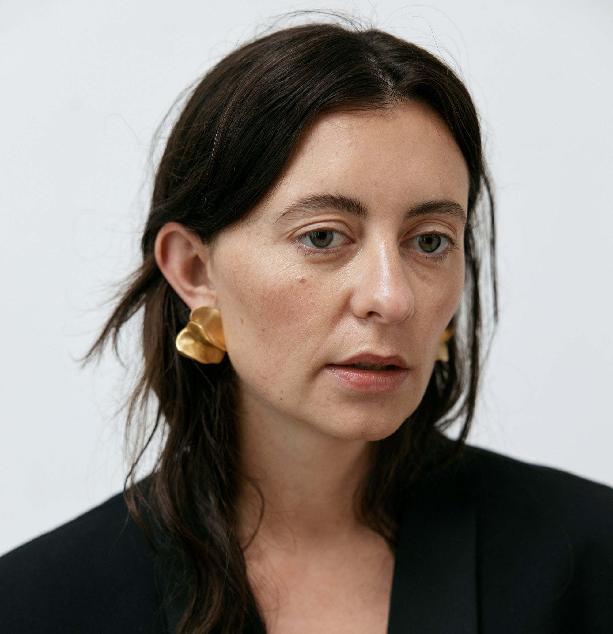 Woman wearing gold earrings against a plain background