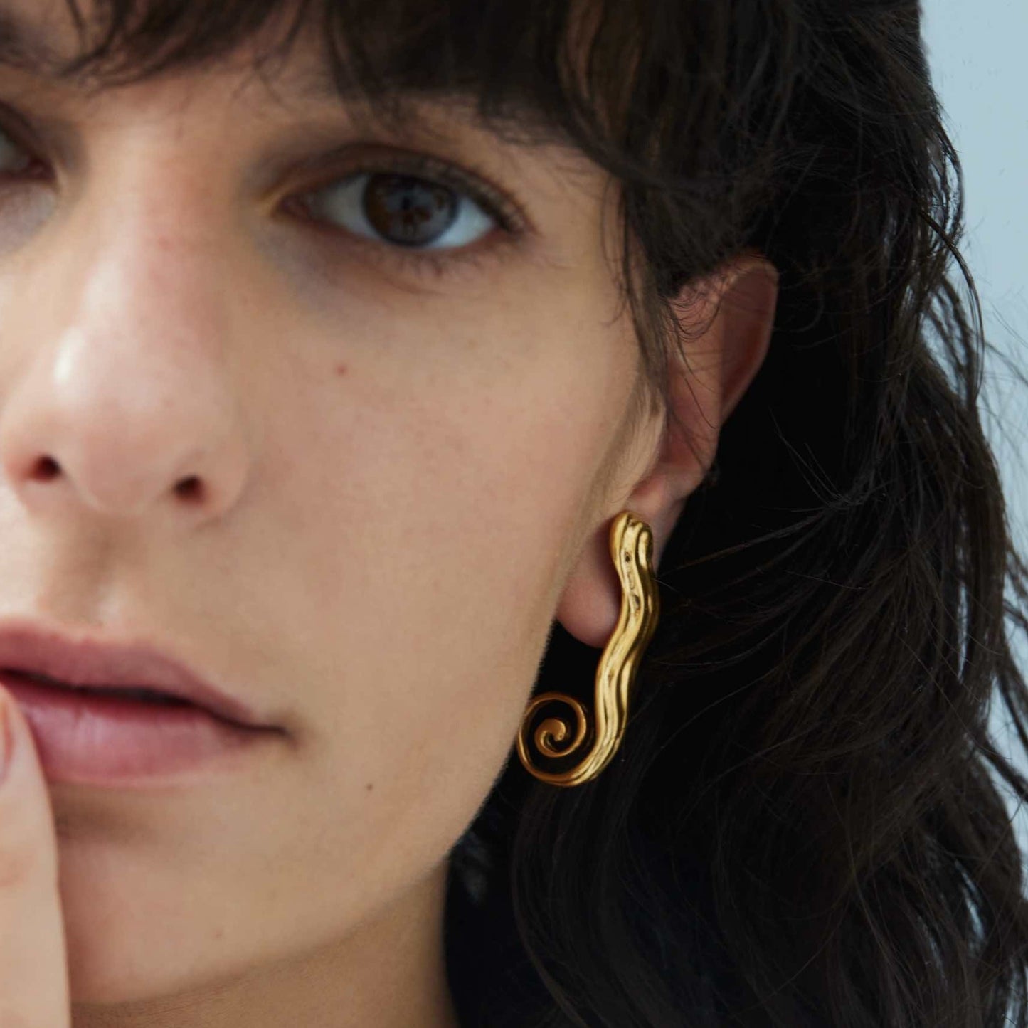 Close-up of model wearing wavy gold earrings