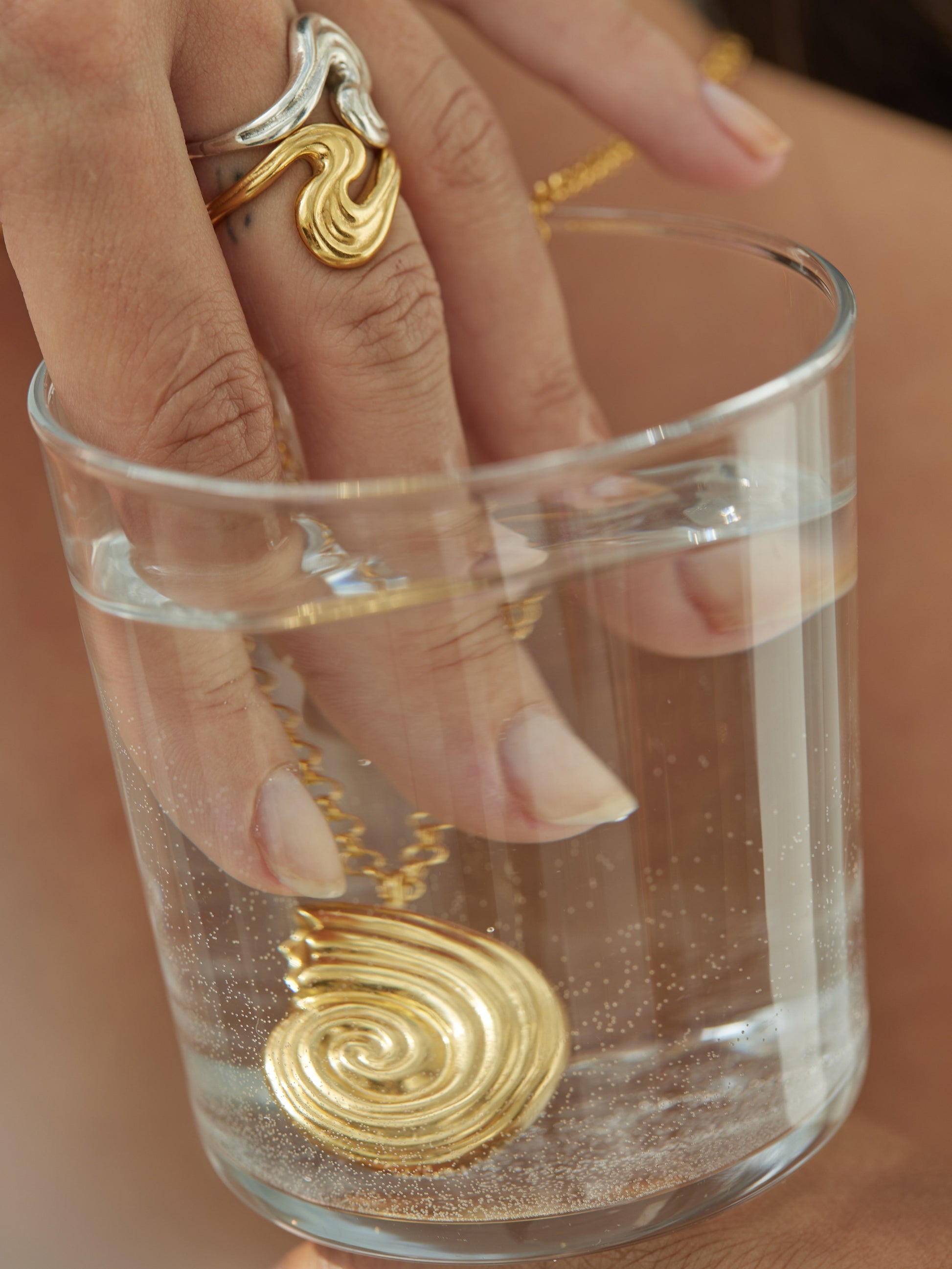 Hand with rings putting fingers and necklace in a glass of water