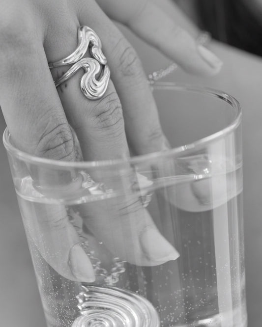 Hand with rings putting fingers and necklace in a glass of water