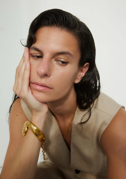 Model wearing a large, sculptural gold bracelet
