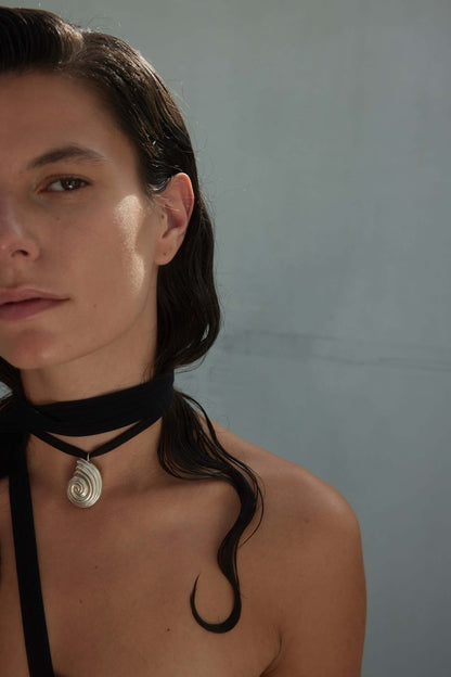 Model with curled hair wearing large silver necklace