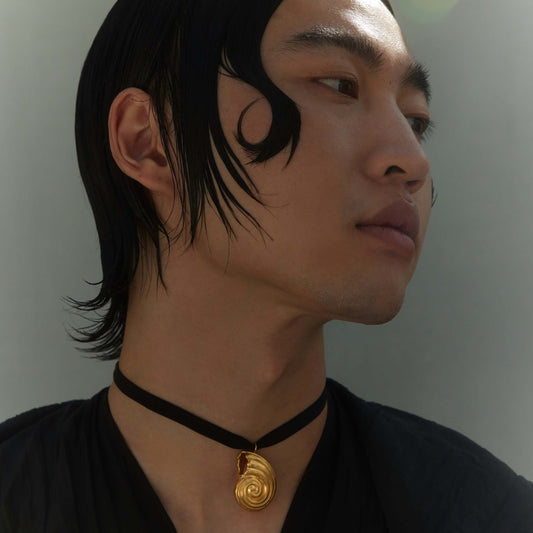 Male model wearing gold pendant with black silk ribbon