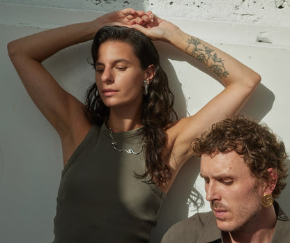 Two models standing in the sun against a wall, wearing gold and silver jewelry