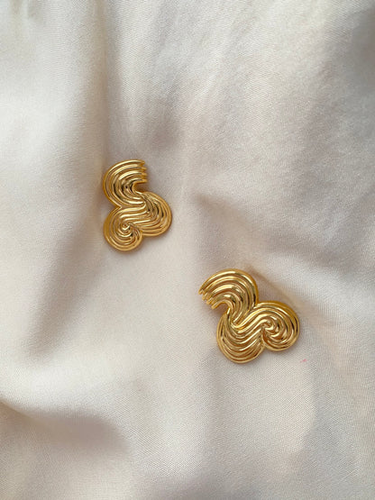 A pair of gold-toned, textured spiral stud earrings resting on a draped white fabric background.