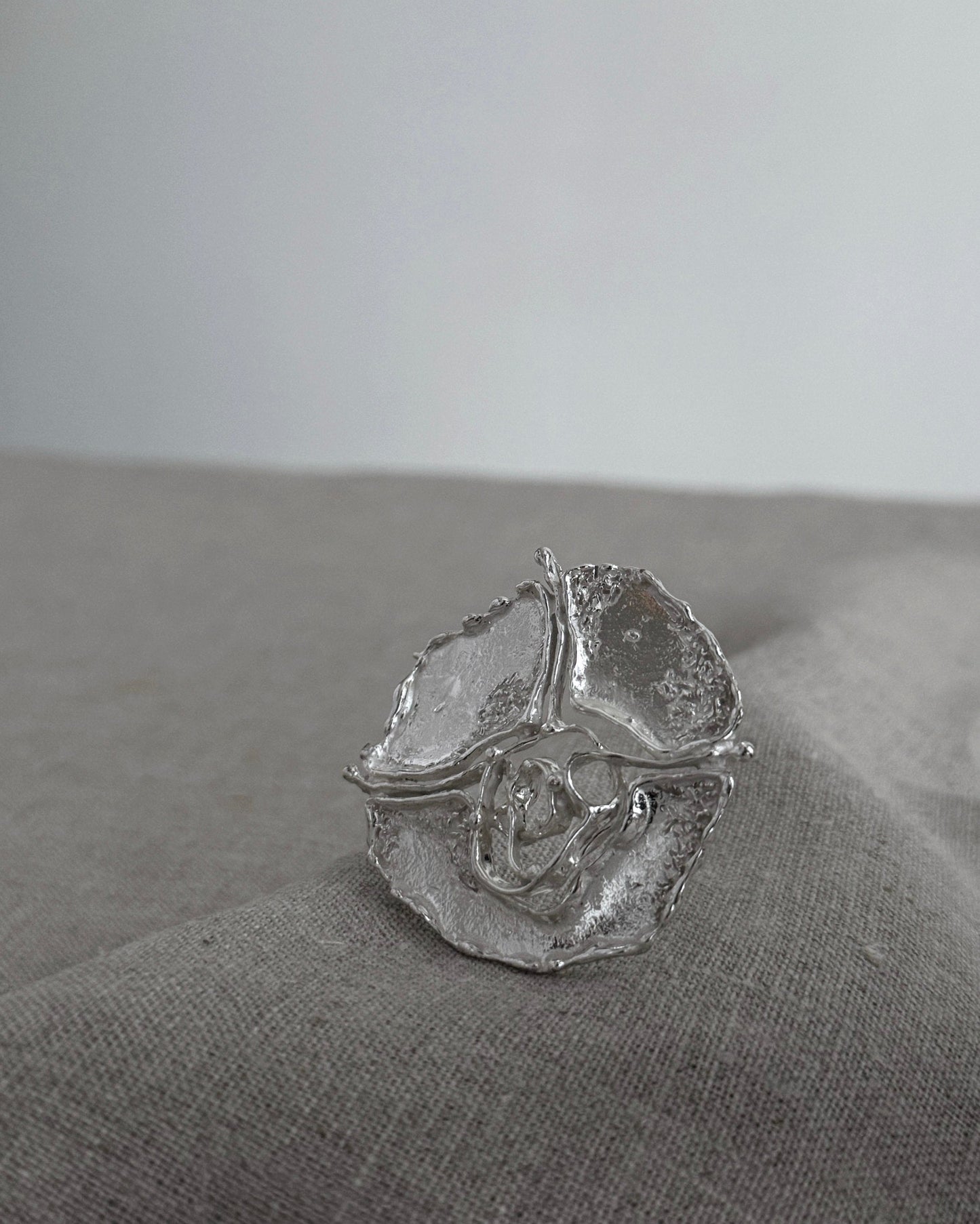 Silver brooch with a textured design on a gray fabric surface