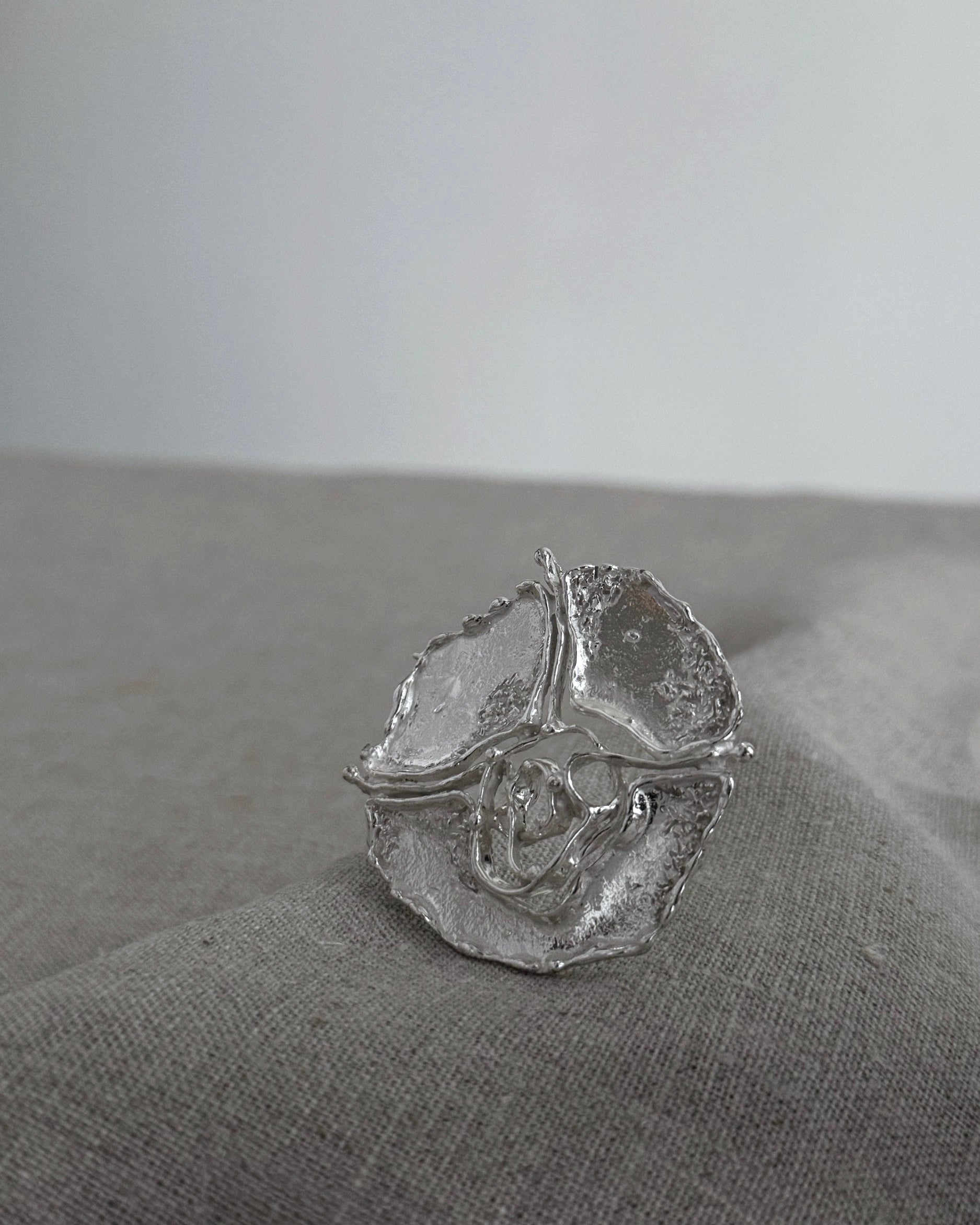 Silver brooch with a textured design on a gray fabric surface