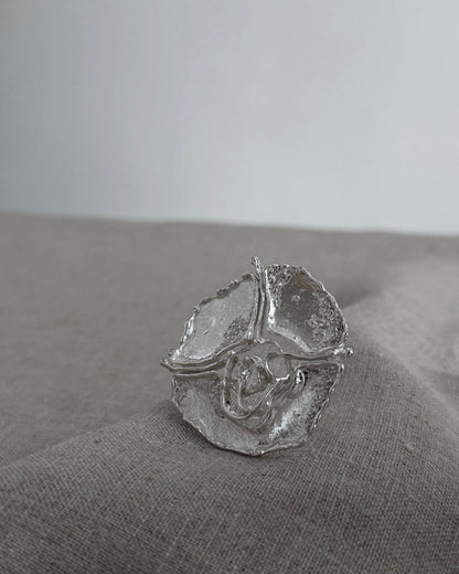 Silver brooch with a textured design on a gray fabric surface