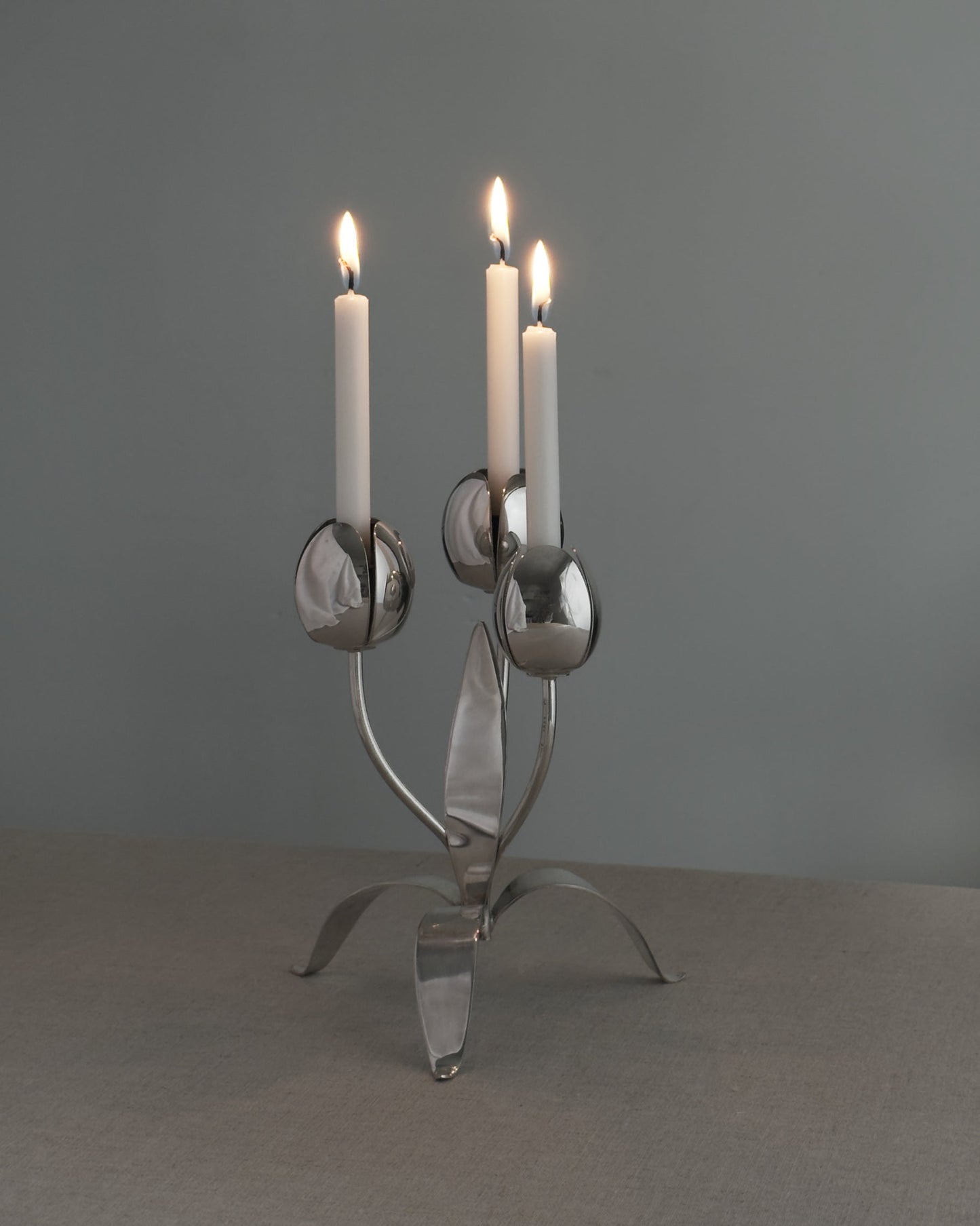 Silver candelabra with three lit candles on a gray background
