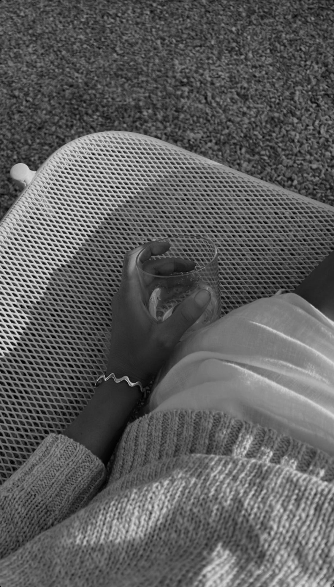 Black and white photo of a hand resting on a chair, wearing a bracelet