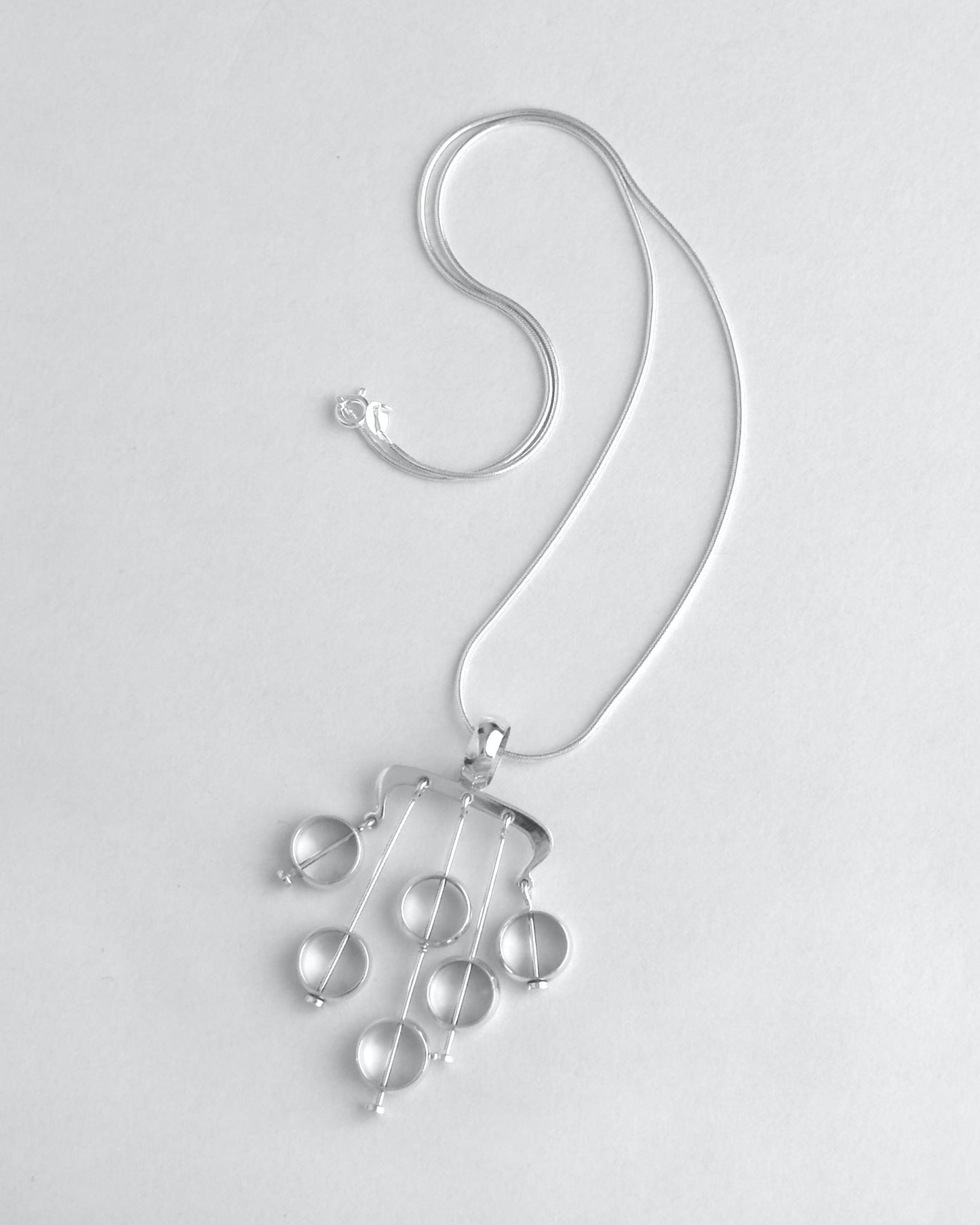 Silver necklace with hanging droplet pendants on a light gray background