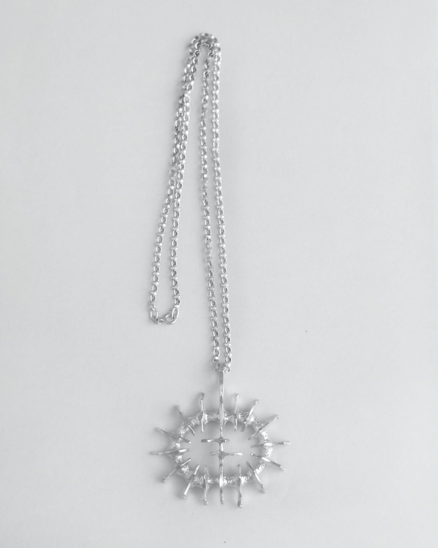 Silver necklace with a large sculptural pendant on a light gray background