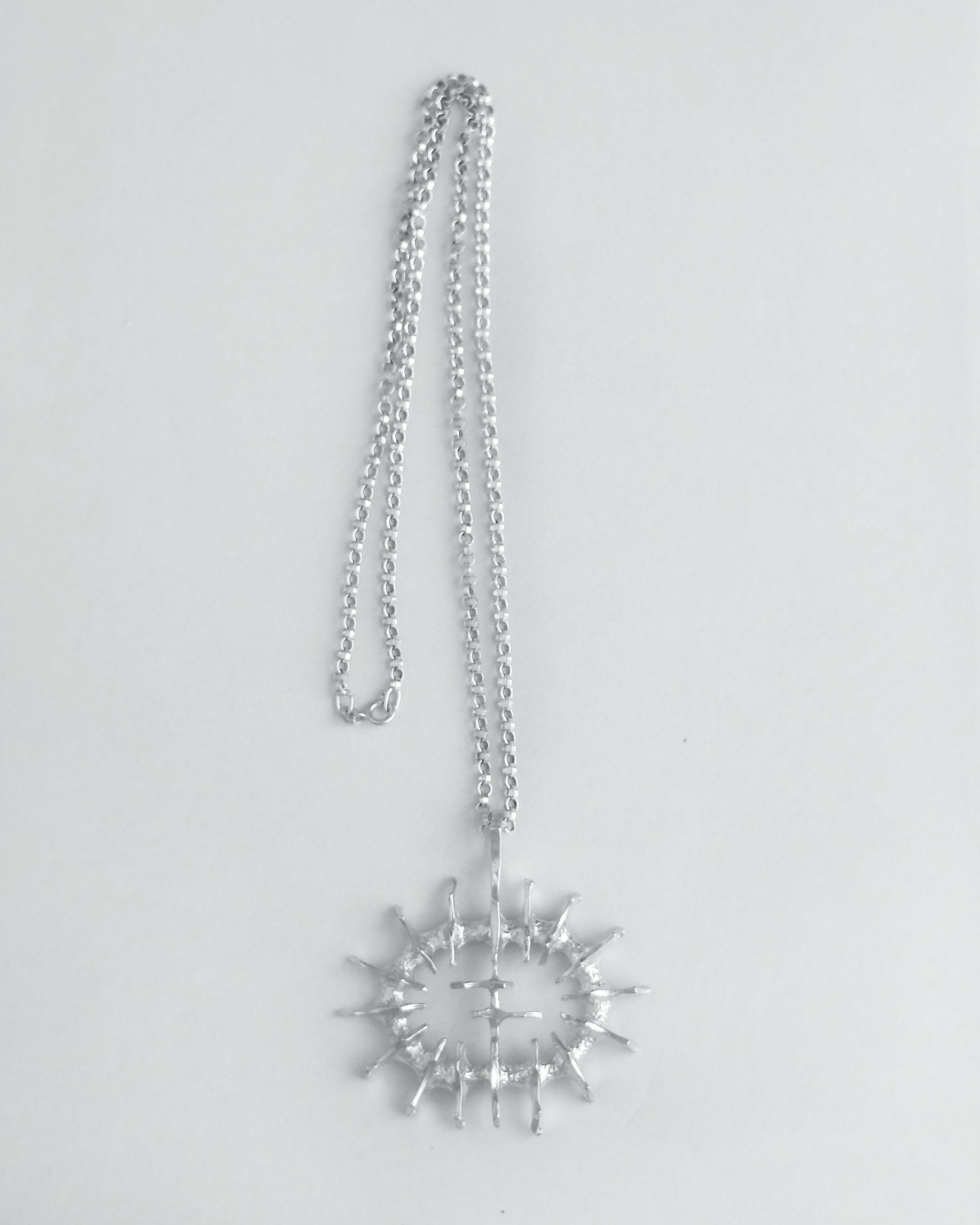 Silver necklace with a large sculptural pendant on a light gray background