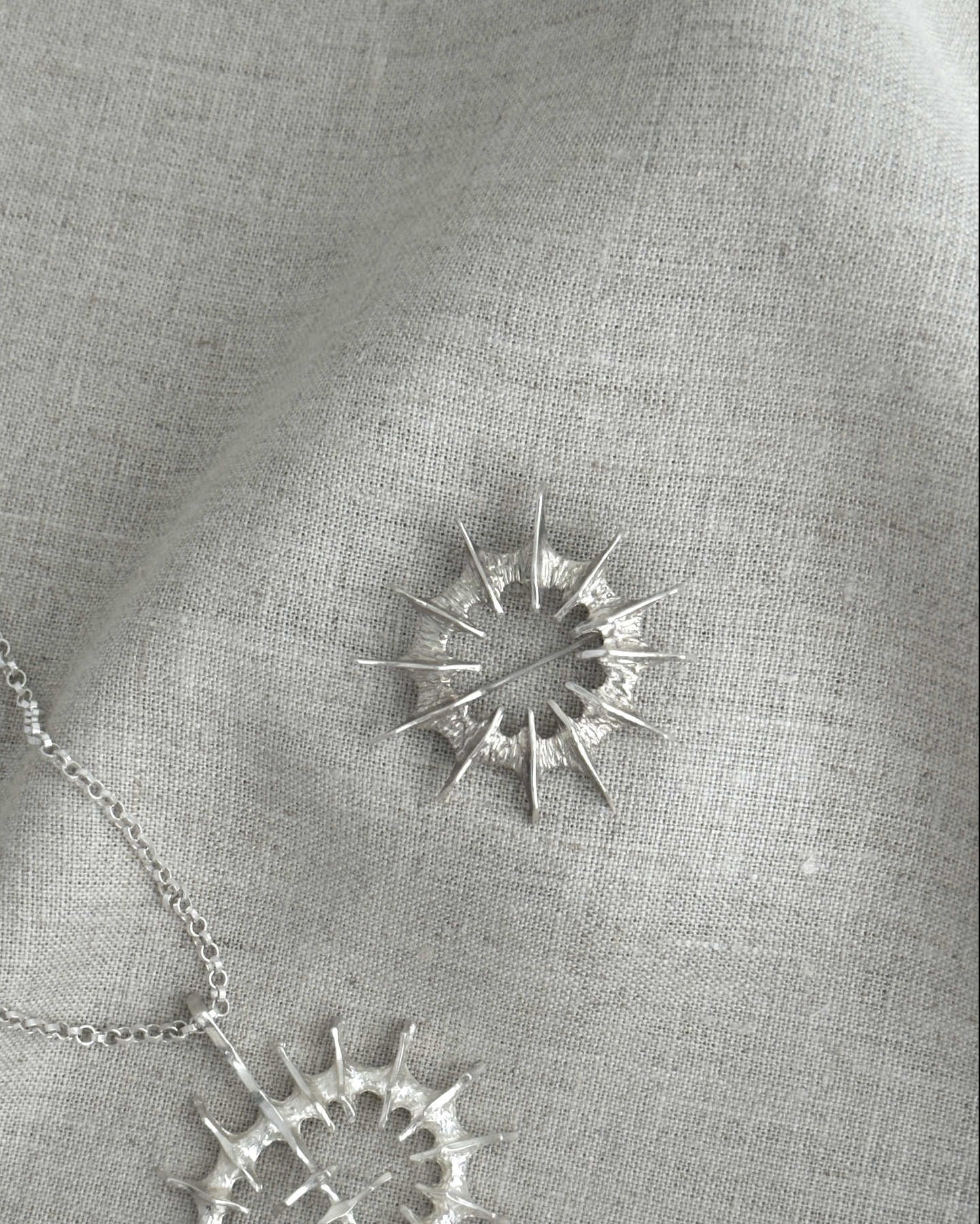 Silver necklace and a brooch on a gray fabric background