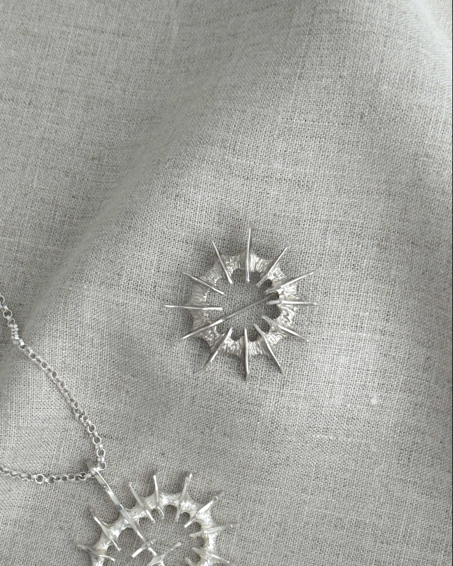 Silver necklace and a brooch on a gray fabric background