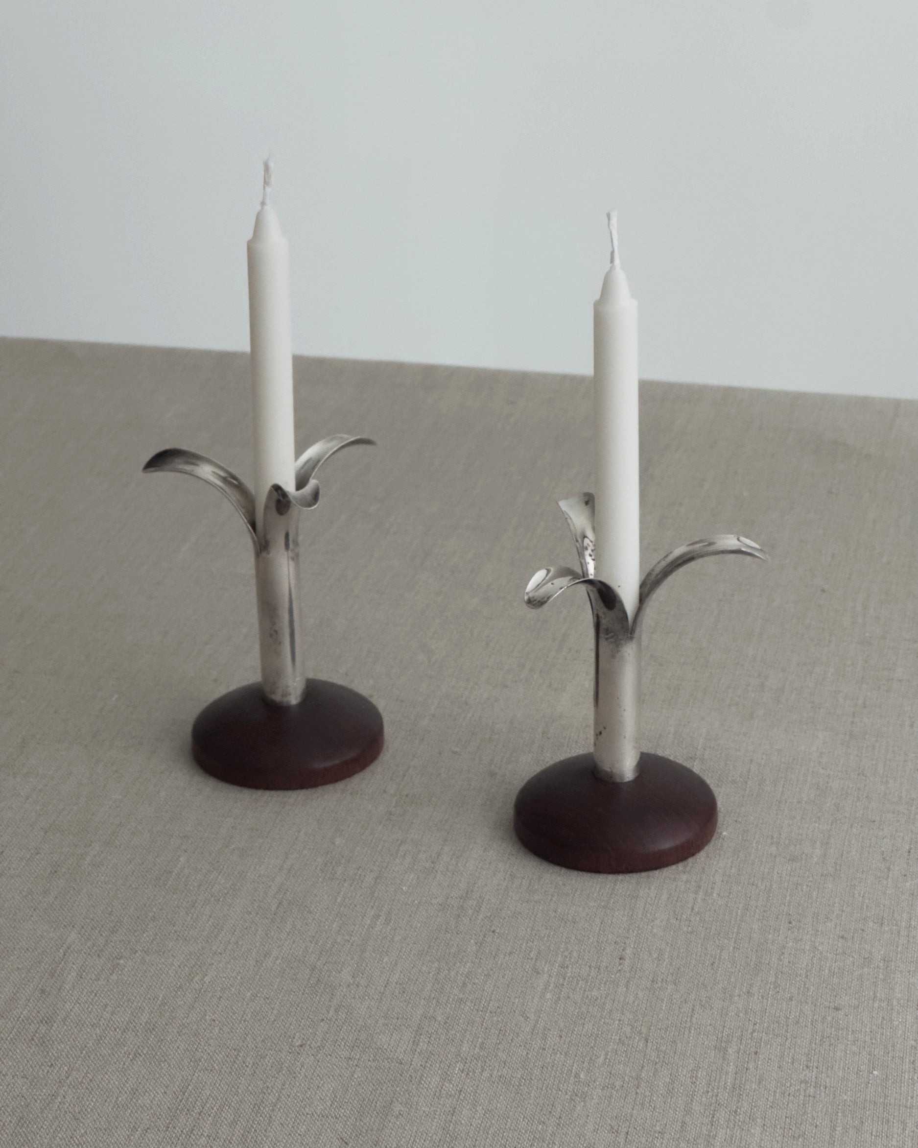 Two metal candle holders with candles on a neutral surface