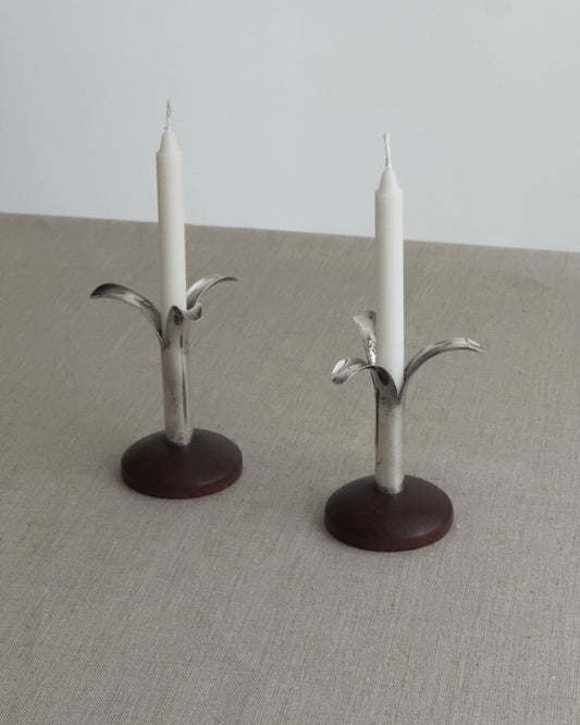 Two metal candle holders with candles on a neutral surface