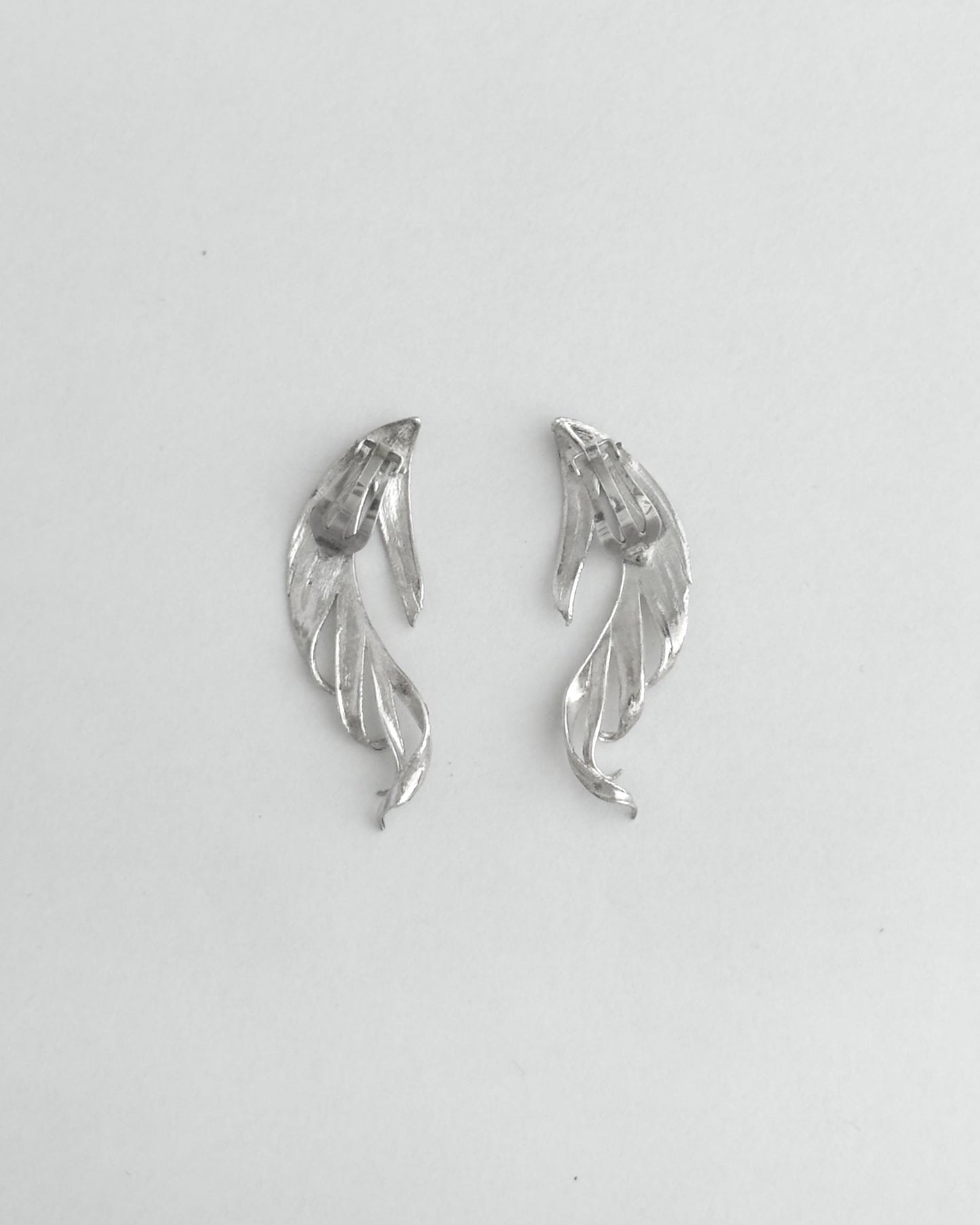 Pair of silver leaf-shaped earrings on a light gray background