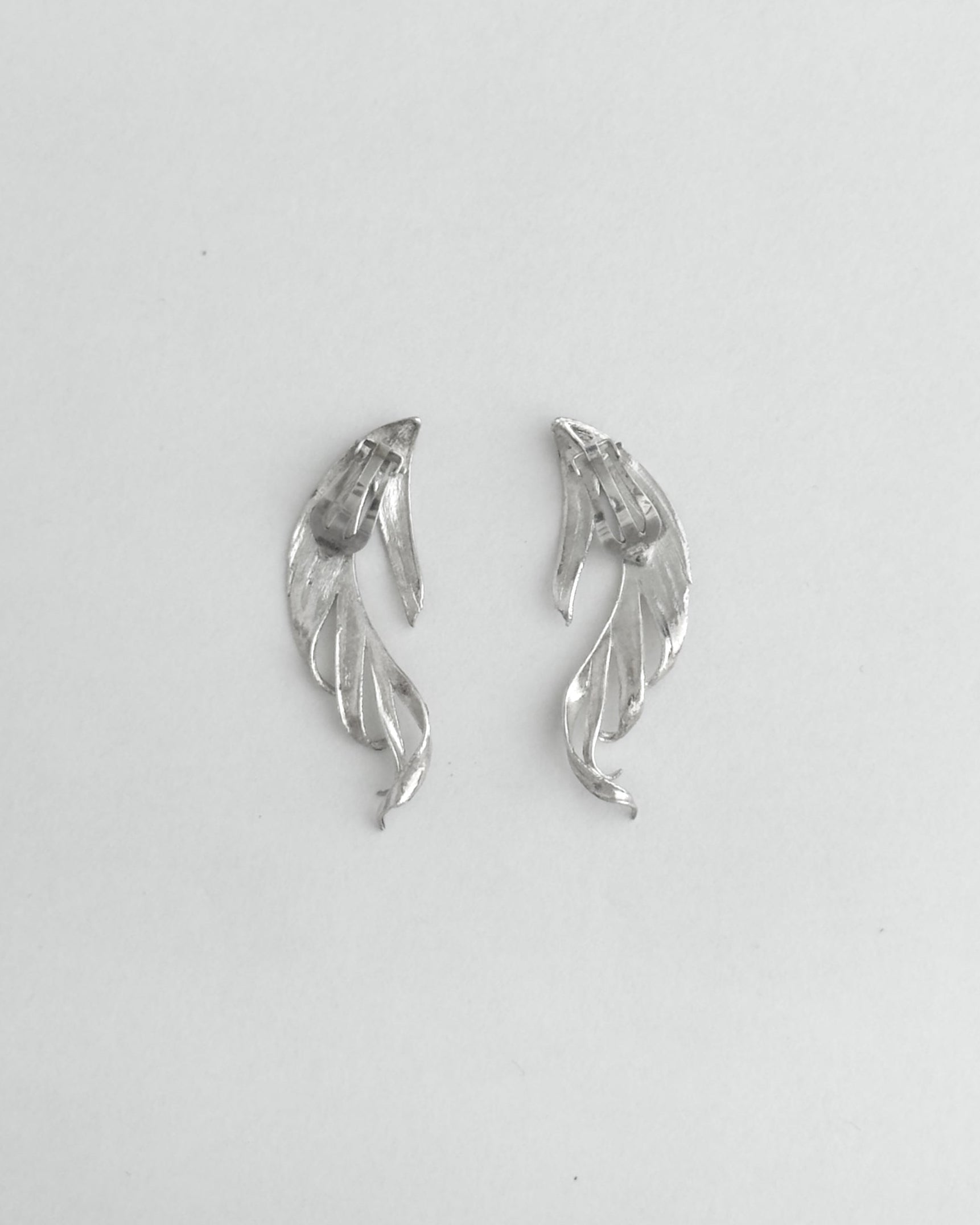 Pair of silver leaf-shaped earrings on a light gray background