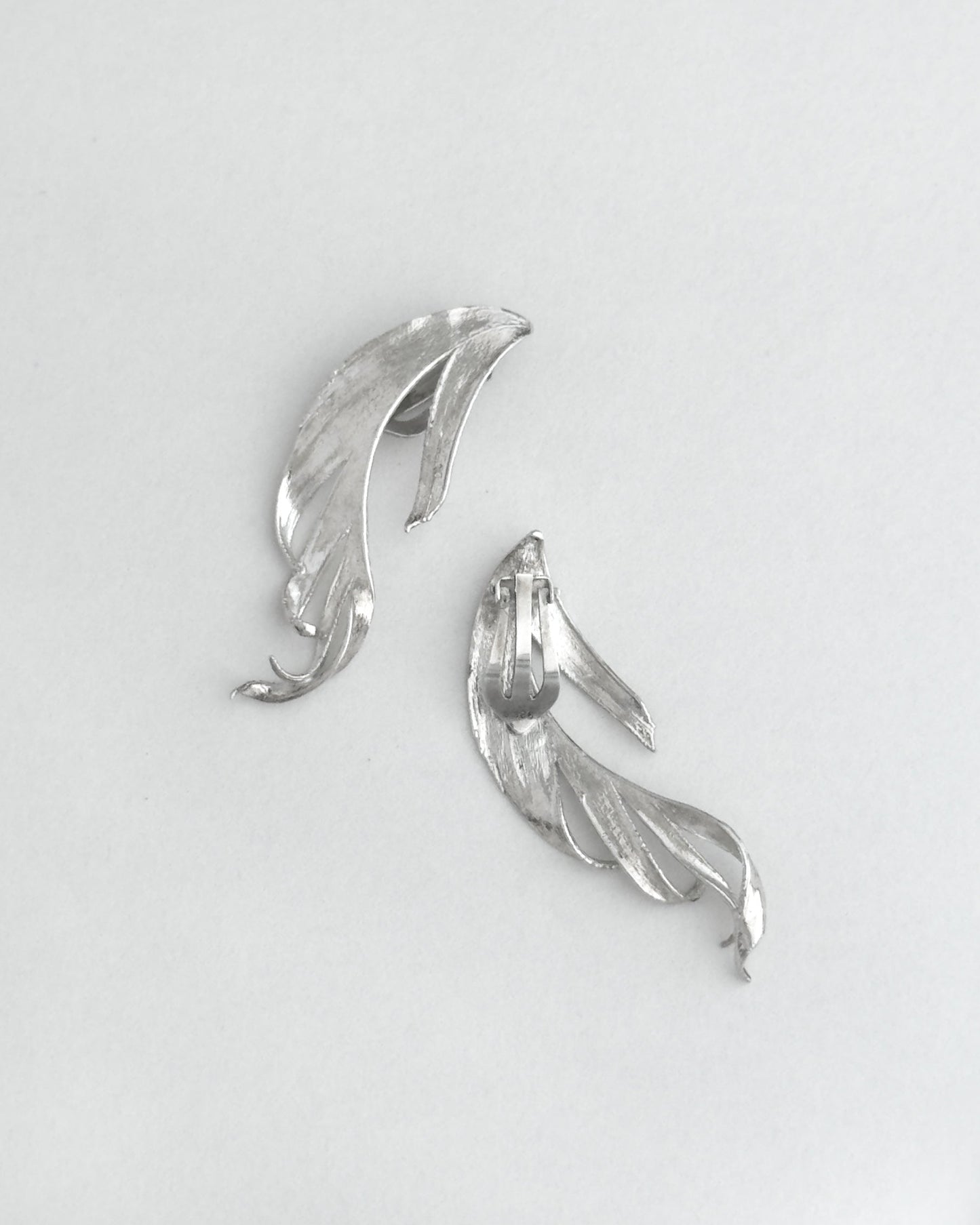 Silver leaf-shaped earrings on a light gray background