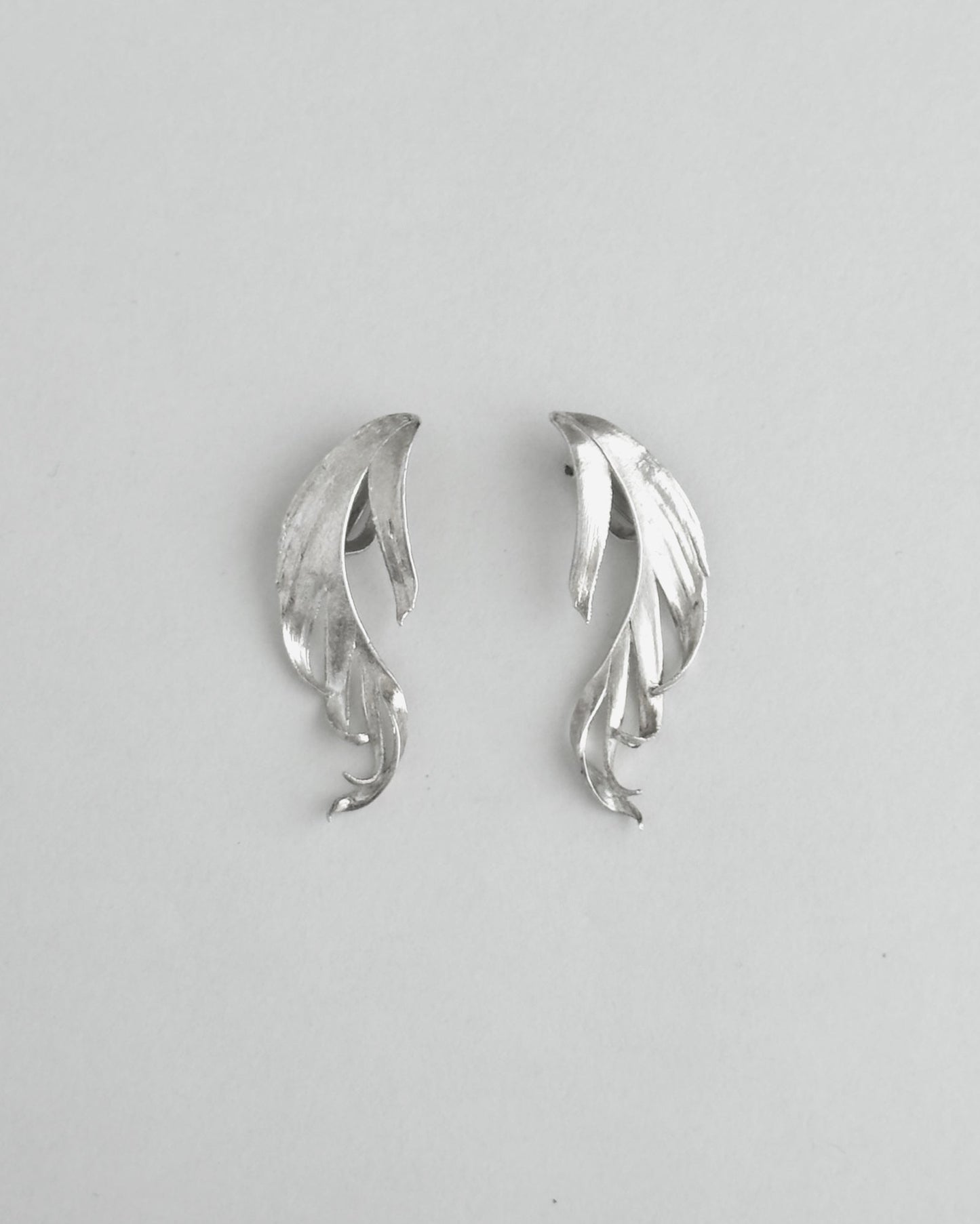 Pair of silver leaf-shaped earrings on a light gray background