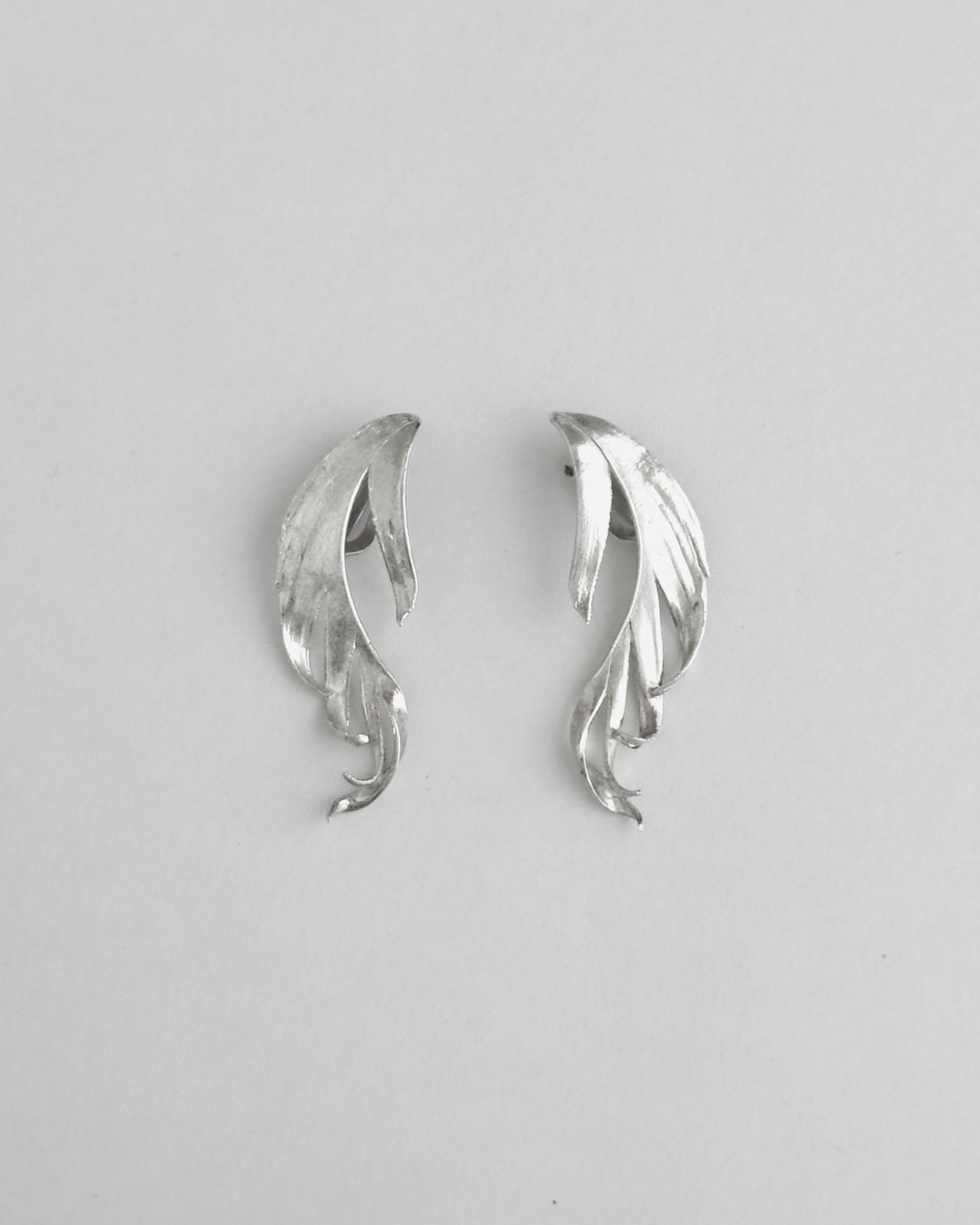 Pair of silver leaf-shaped earrings on a light gray background