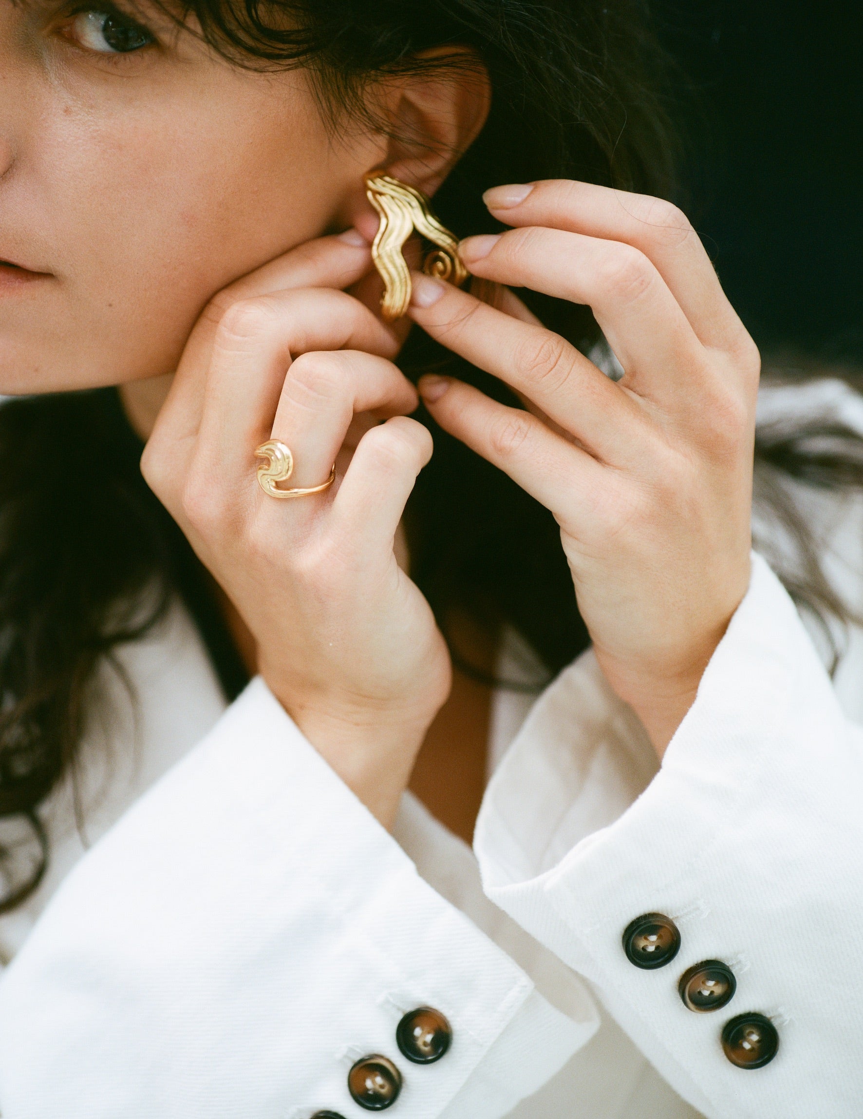 Model wearing wavy gold earrings, touching them with both hands