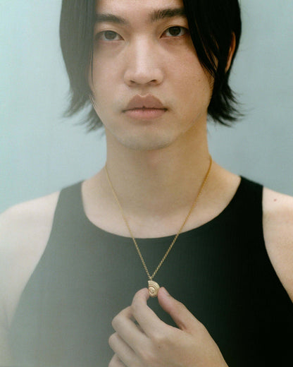 Male model wearing gold necklace, holding the pendant with two fingers