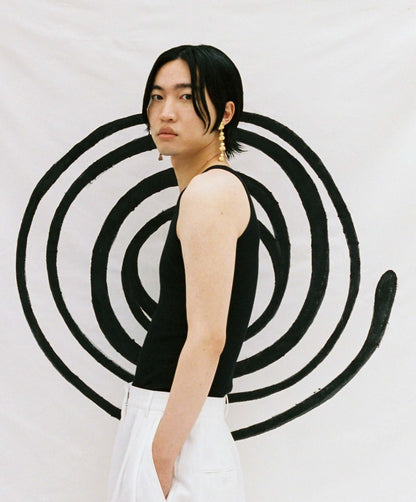 Male model wearing drop earring in gold, in front of a large painted spiral