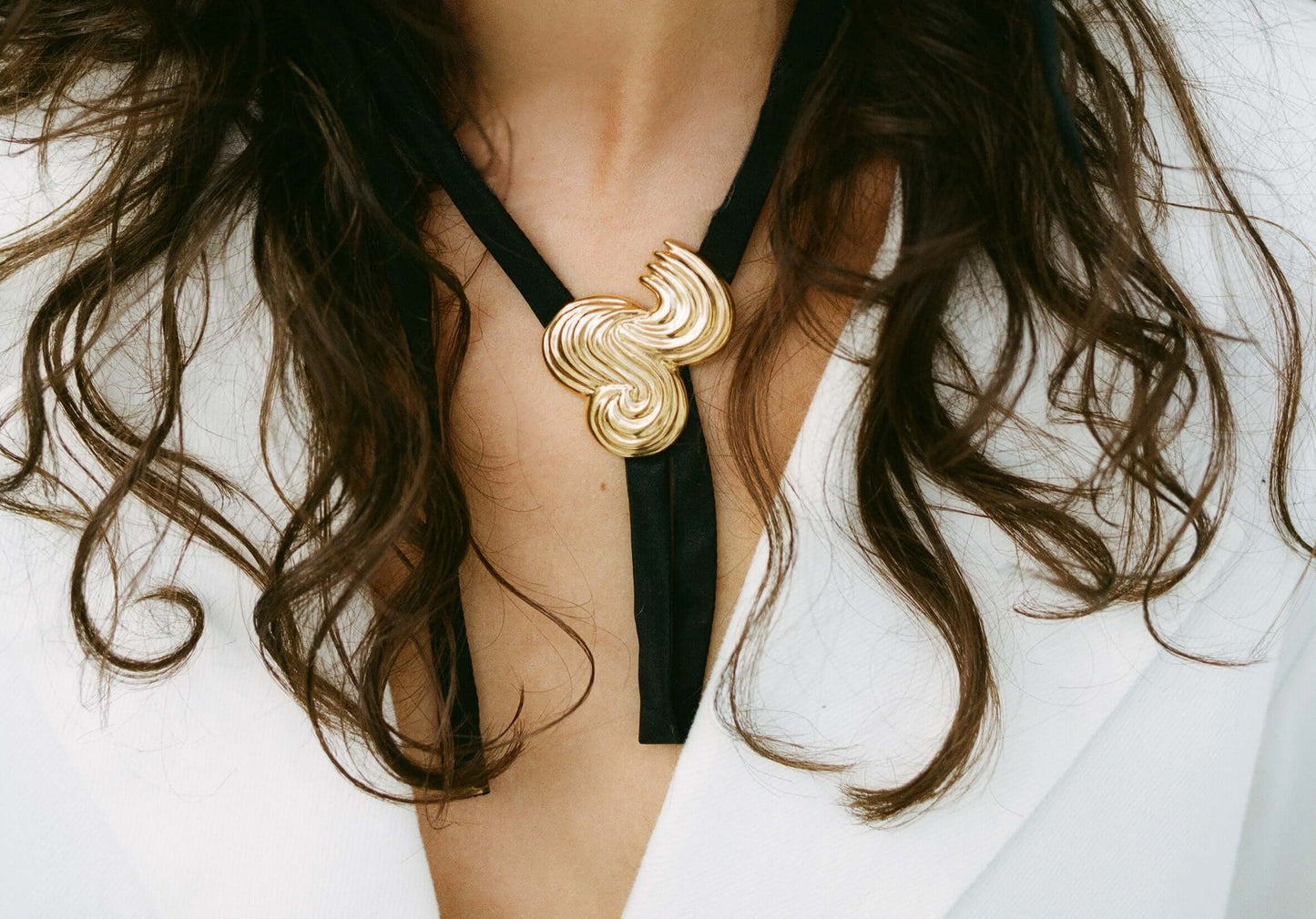Models neck wearing gold necklace with silk ribbon. 
