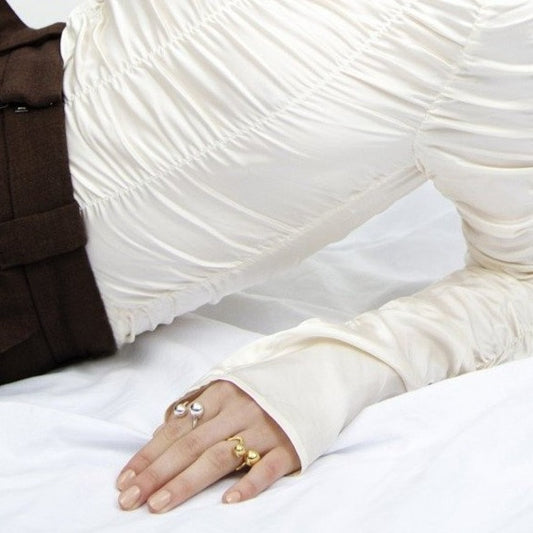 Woman sitting on the floor, leaning backwards. Wearing white blouse and rings