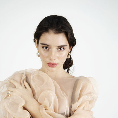 Woman looking into camera, wearing transparent pink garment and silver earrings