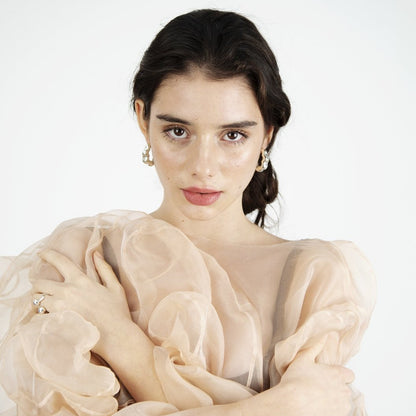 Woman looking into camera, wearing transparent pink garment and silver earrings