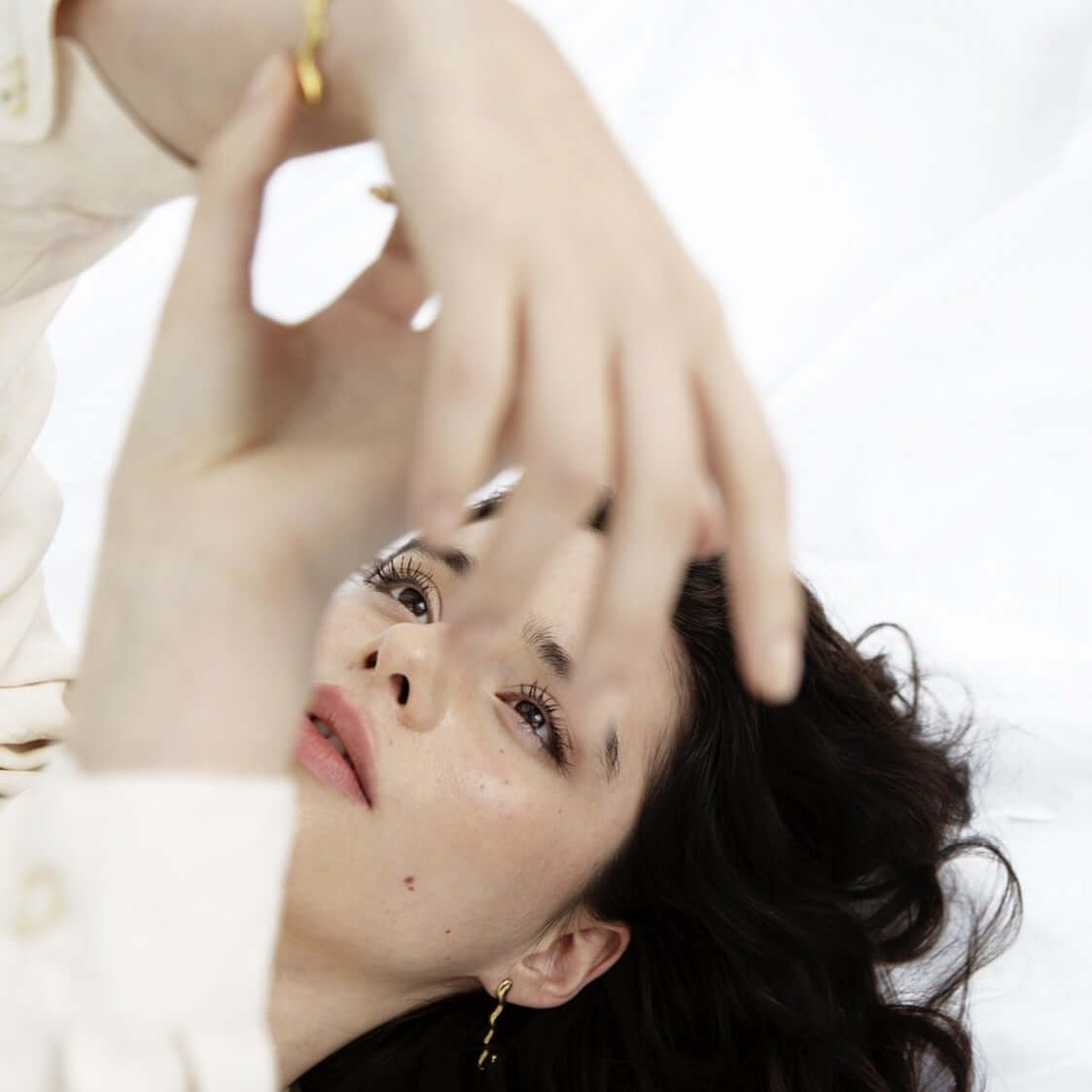 Woman lying on the floor, playing with her bracelet. Wearing white blouse and jewelry