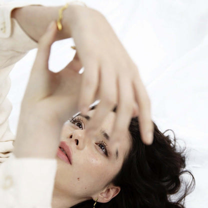 Woman lying on the floor, playing with her bracelet. Wearing white blouse and jewelry